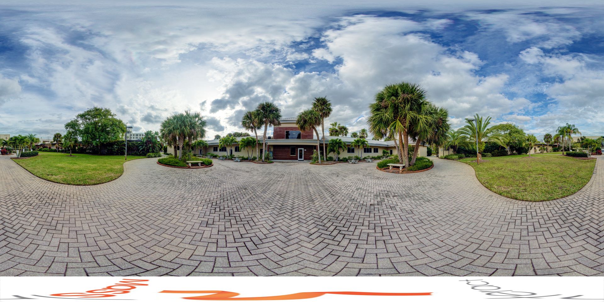 Panoramic view of the Academic Quad, featuring a paved pathway leading to a classic building flanked by lush palm trees under a spacious sky